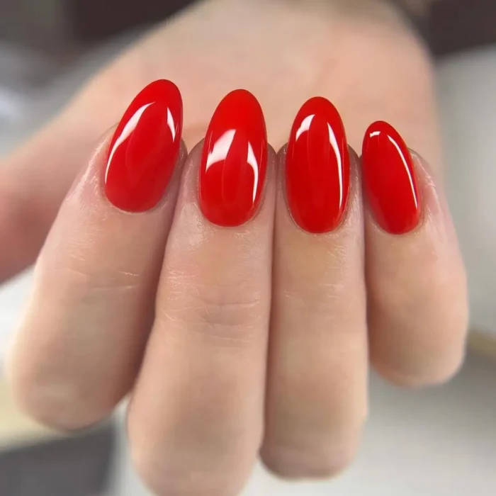 A close-up shot of a hand showcasing a flawless, glossy red manicure on medium-length oval nails.