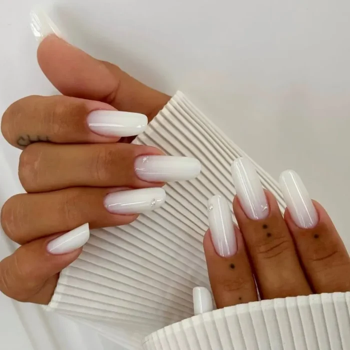 Hands showing a simple white nail idea with a soft ombré effect and tiny silver glitter accents on long nails.