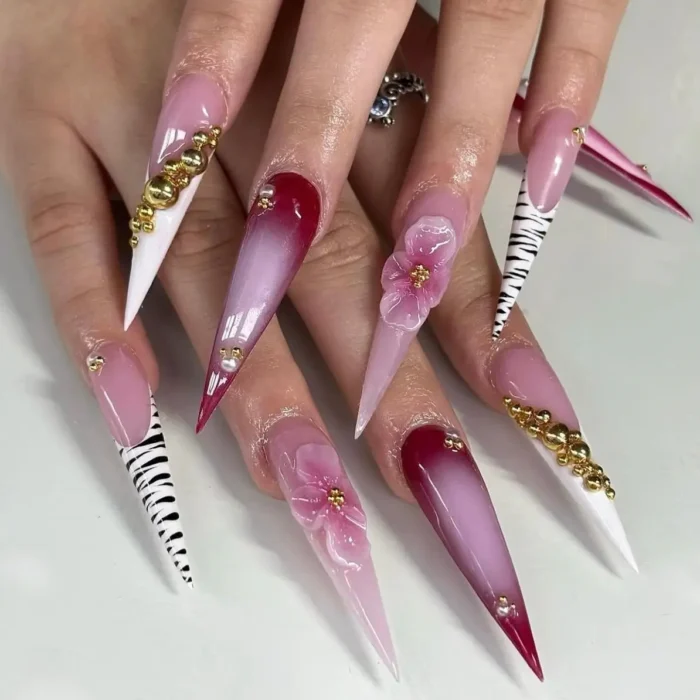 Bold pink and red stiletto nails with zebra print, 3D flowers, and gold hardware.