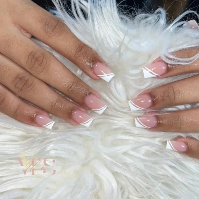 Hands showing a simple white nail art design with a double-lined, graphic V-shaped French tip.