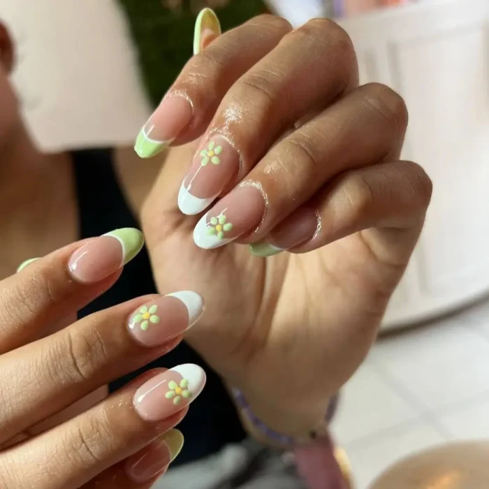 A close-up of a simple oval nail design featuring a French manicure with daisy accents and pastel green tips.