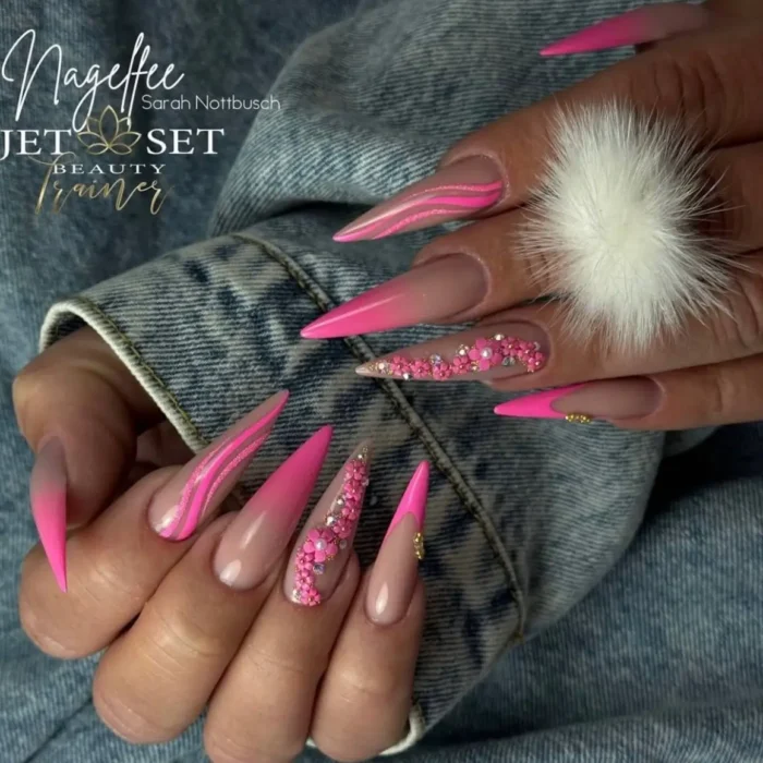 A fun hot pink stiletto nail design with crystal accents, glitter lines, and a pom-pom charm.