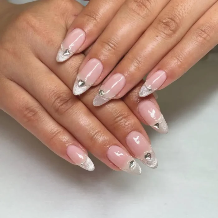 Almond nails featuring a silver glitter V-french tip with a silver heart charm accent.