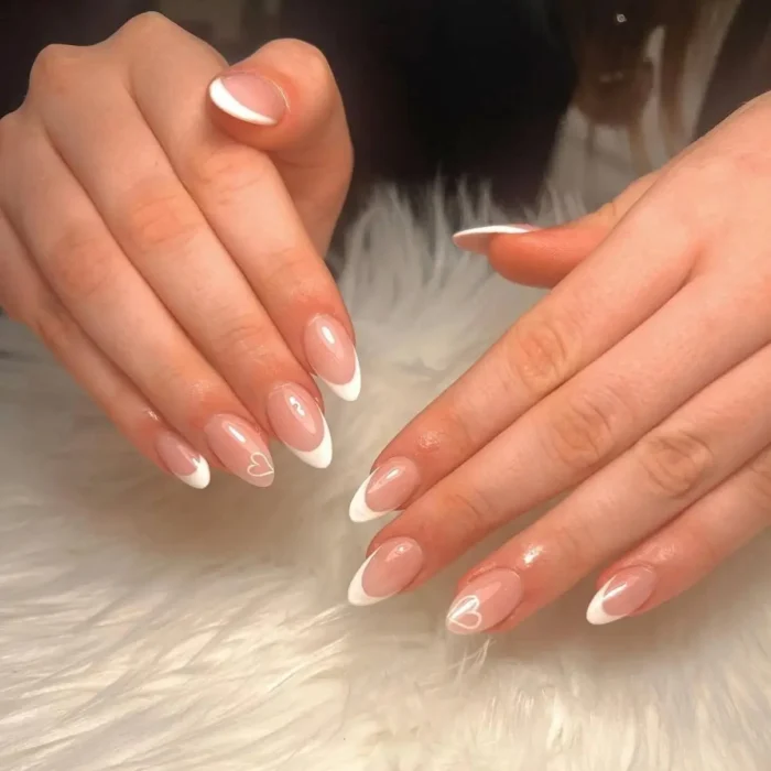 A simple white nail idea showing a French manicure on almond nails with a delicate heart outline accent.