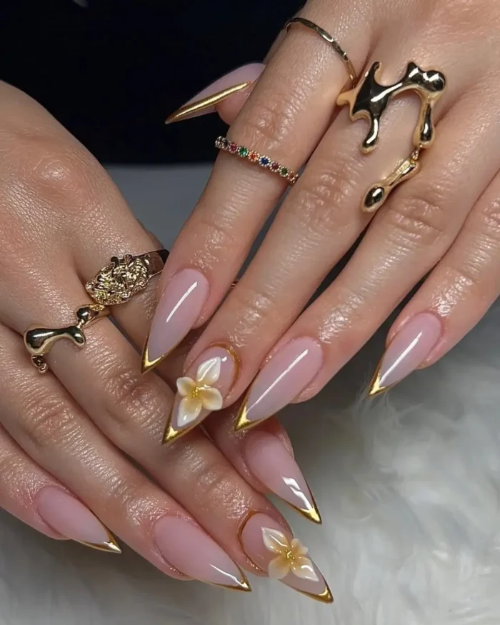 Medium nude stiletto nails with gold outlines, accented with 3D white and yellow flowers and small pearls.