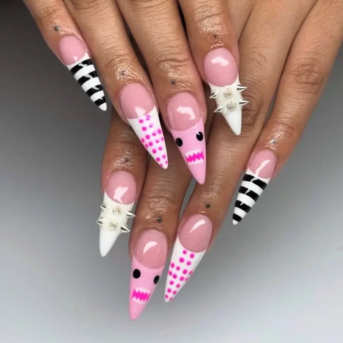Funky pink stiletto nails with shark characters, stripes, and silver spikes.