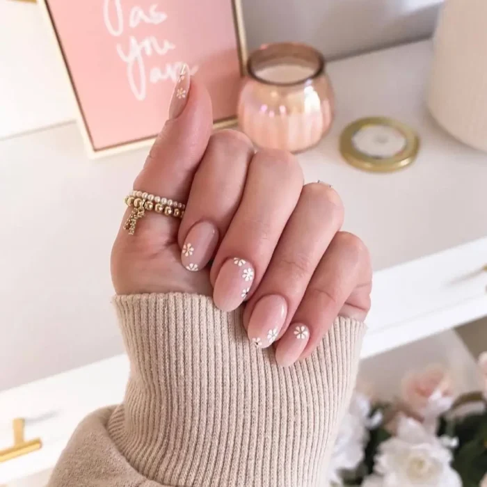 A hand with a simple design on short oval nails, featuring a sheer nude base with scattered daisy nail art.