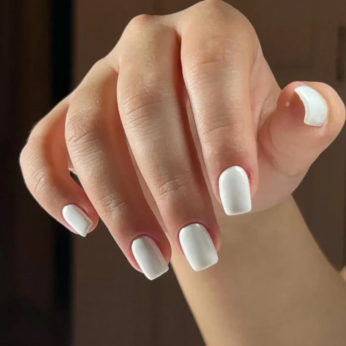 A hand with short, square nails painted in a crisp, simple white nail design.