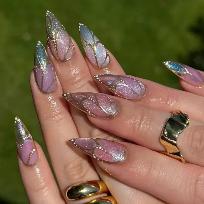 Long stiletto nails with iridescent lavender, pink, and blue, outlined in gold to resemble butterfly wings with small white dots.