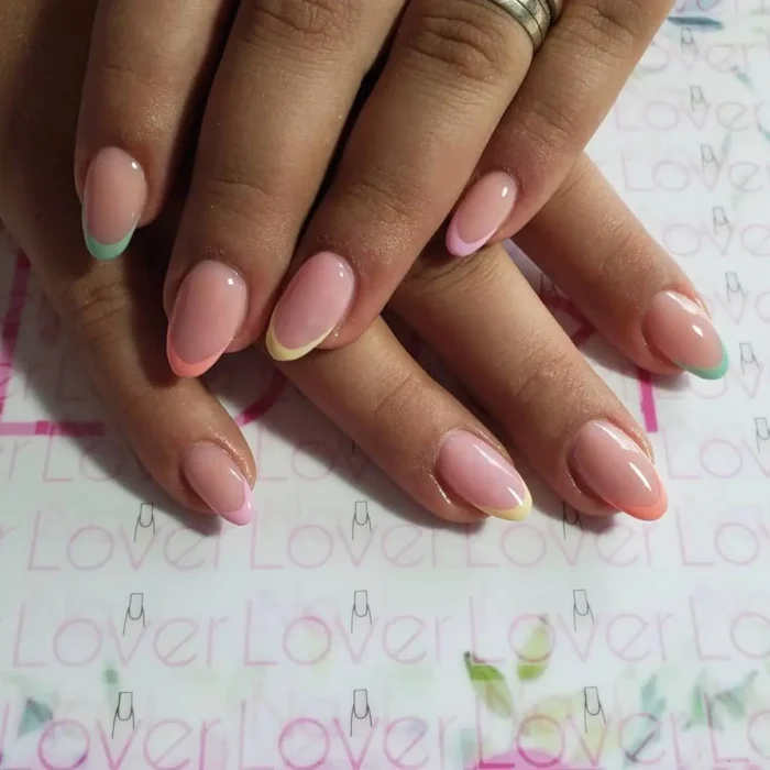 A simple oval nail design featuring a modern French manicure with mismatched pastel-colored tips.