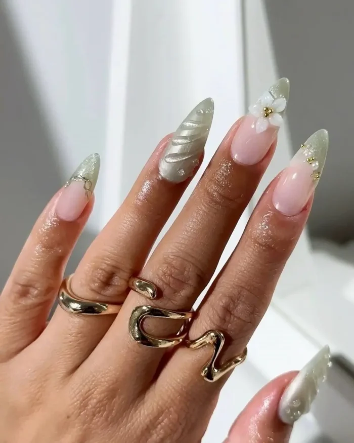 A detailed look at mismatched stiletto nails with sage green cat eye tips, 3D flowers, and textured accents.