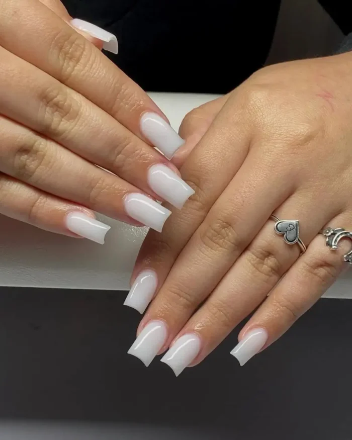 A simple white nail design in a milky color on nails with a unique curved square tip shape.