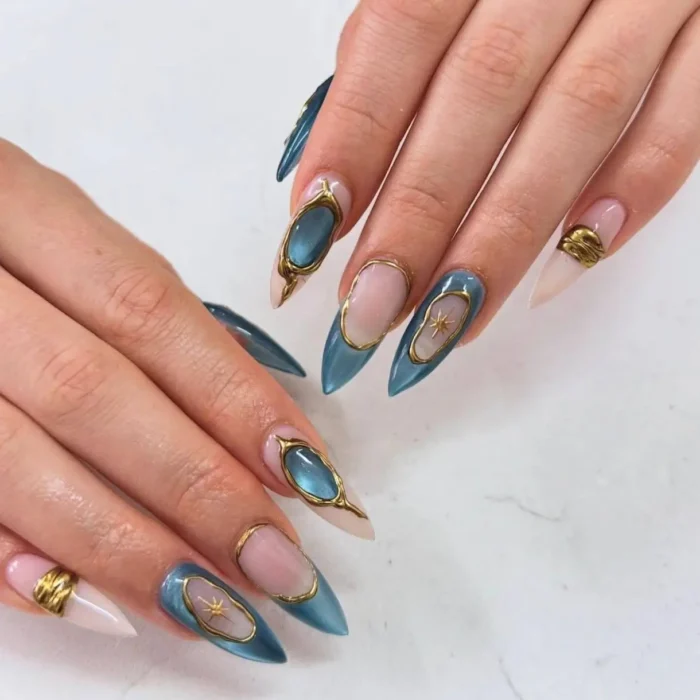 Long stiletto nails with translucent blue and nude sections, featuring raised gold frames, gold bands, and gold star charms.