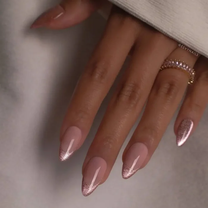 A close-up of elegant almond nails with a delicate rose gold glitter french tip.