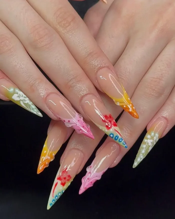 Long stiletto nails with pastel yellow, orange, and pink tips, decorated with 3D flowers and small raised dots.