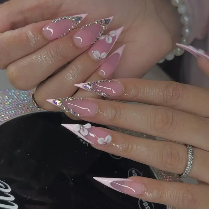 Elegant light pink stiletto nails with a rhinestone frame and 3D white flowers.