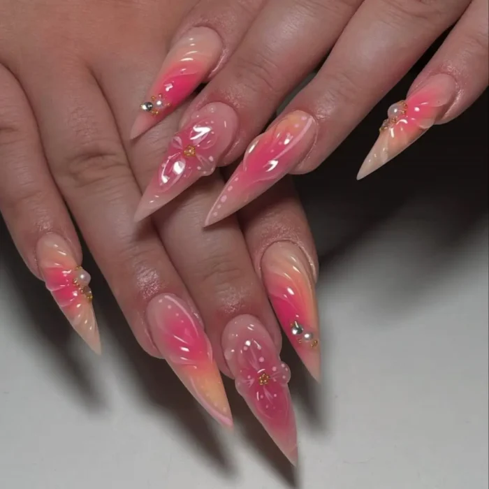 Artistic pink stiletto nails with a jelly bloom effect, 3D flowers, and pearl details.