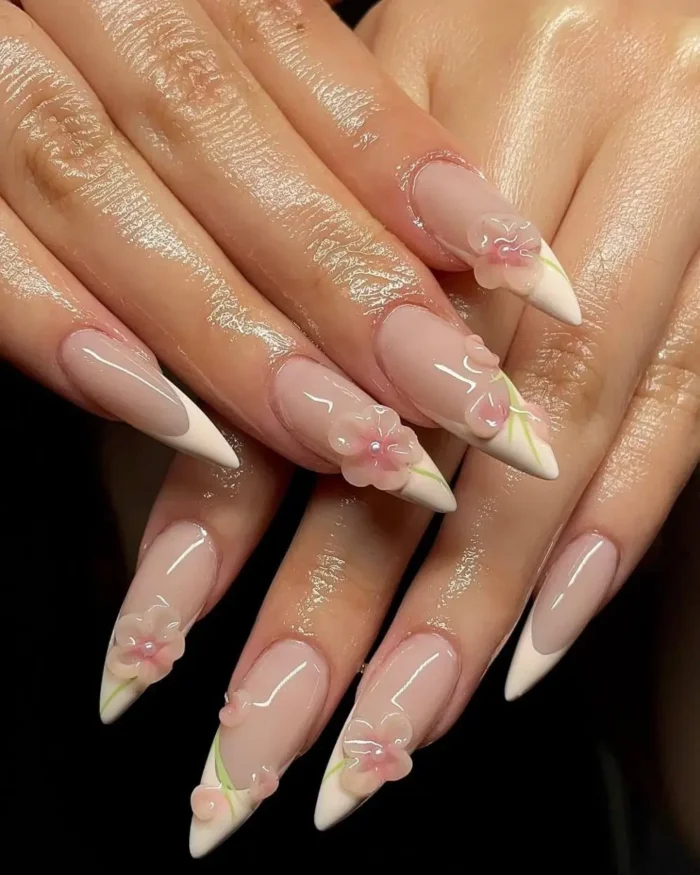 Long stiletto nails with white French tips, decorated with 3D pink flowers and green leaf details.