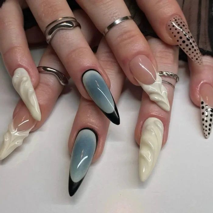 Long stiletto nails with a mix of black polka dots, grey gradients with black tips, and textured white 3D sculpted designs.