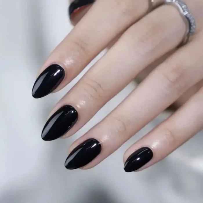 A hand with sleek, medium-length oval nails painted in a simple, high-gloss solid black polish.