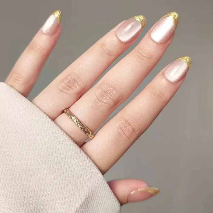 Elegant almond nails with a pearlescent cat eye base and a textured gold french tip.