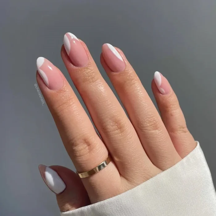 A hand showing almond-shaped nails with a simple white nail art design of modern abstract curves on a natural base.