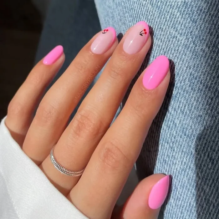 A hand showing a manicure with bright pink nails and two accent nails featuring a simple, tiny cherry design.
