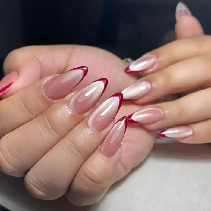 Almond nails with a pearlescent cat eye effect and a thin red french tip outline.