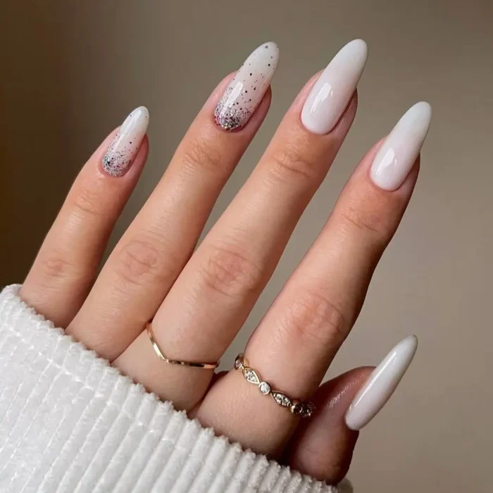 A hand with long almond nails featuring a simple white nail idea with a subtle glitter fade accent nail.