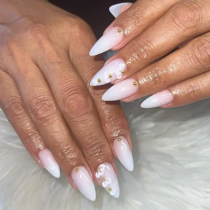 A simple white nail design with a soft ombre effect, accented with 3D white flowers and gold beads.