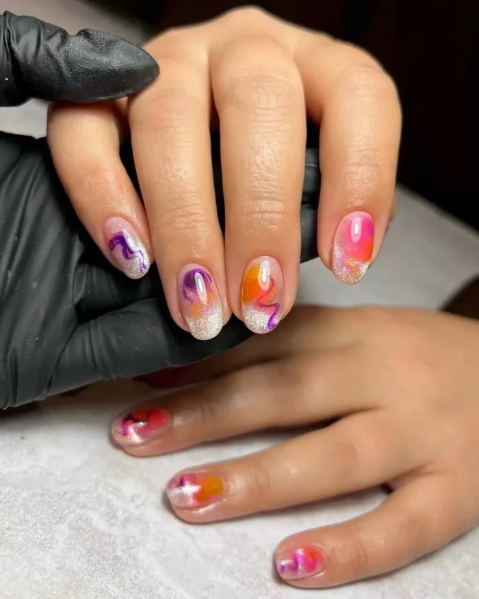 Short nails with a shimmery silver french tip and abstract watercolor swirls of pink and purple.