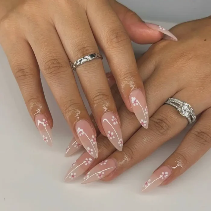 Medium, clear stiletto nails with delicate white cherry blossom designs and pink centers.