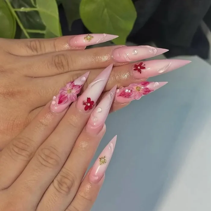 Long pink stiletto nails with a milky ombré base and 3D red flower accents.