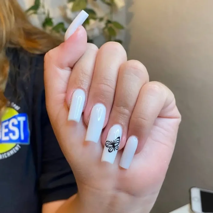 A hand showing a simple white nail design on long square nails with a dainty black butterfly accent art.