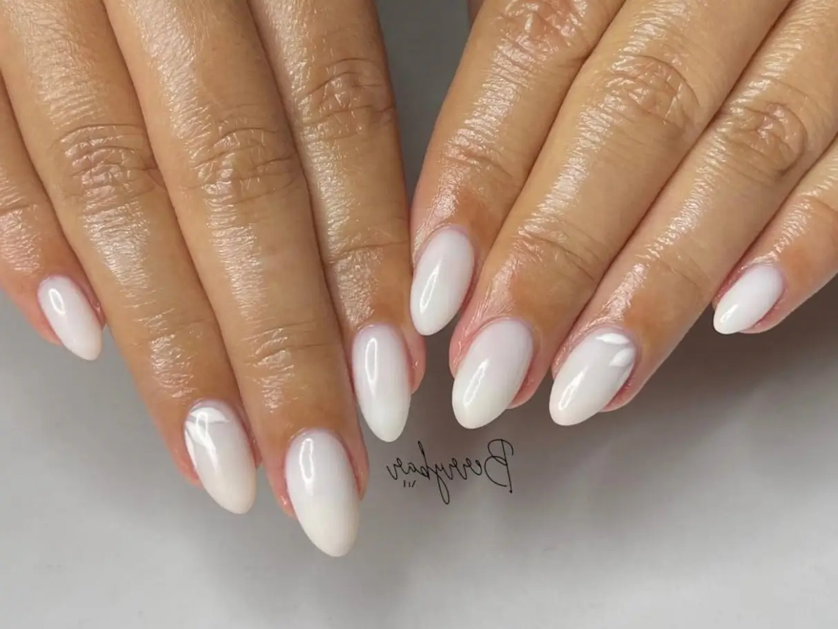 A close-up of a simple oval nail design featuring a milky white base and subtle, tone-on-tone white petal art, representing chic and minimalist nail ideas.